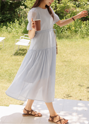 Woman in a light blue dress standing outdoors holding a drink.