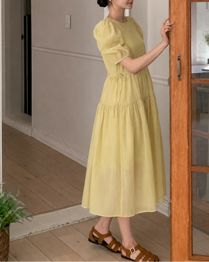 Woman in a yellow dress standing in a home interior.