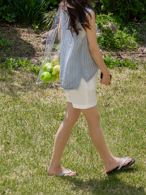 Person walking outdoors with a reusable bag full of apples