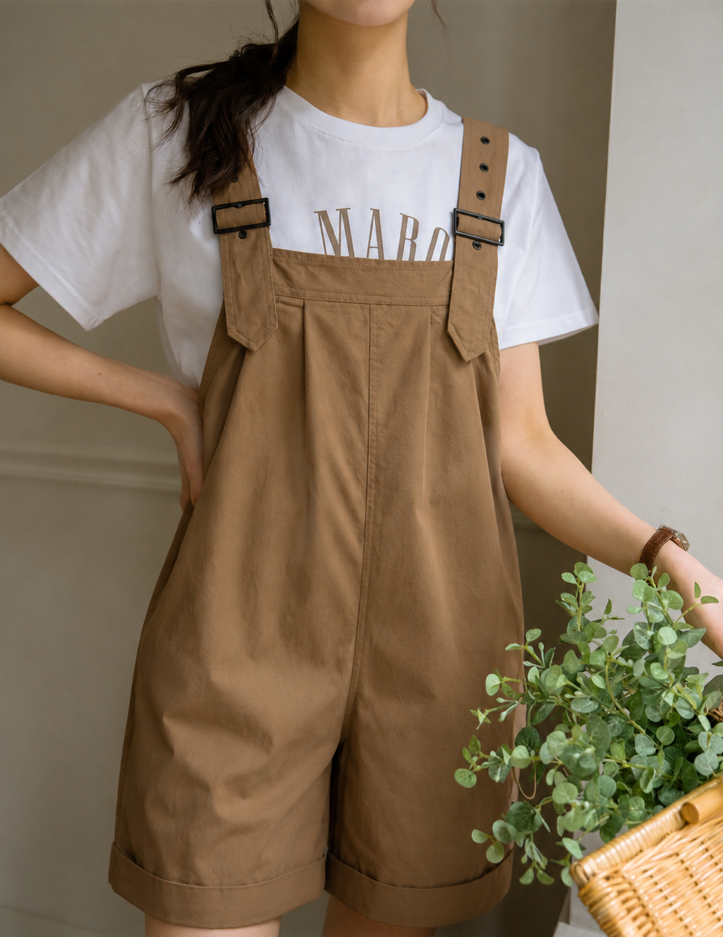 Person wearing a white t-shirt with text and brown overalls, holding a plant.