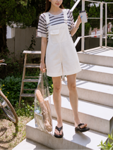 Woman standing on outdoor steps holding a coffee cup and a clear bag.