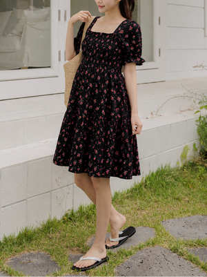 Woman in a black floral dress standing outdoors near a white building.