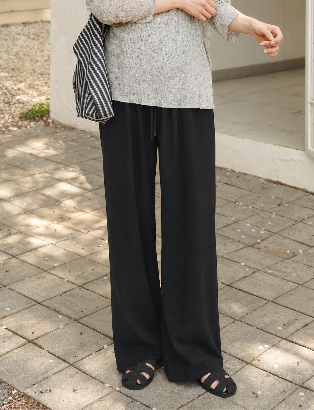 Person wearing a gray top and black wide-leg pants standing on a paved surface.