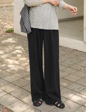 Person wearing a gray top and black wide-leg pants standing on a paved surface.