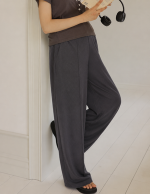 Person wearing a brown top and gray wide-leg pants against a white wall.