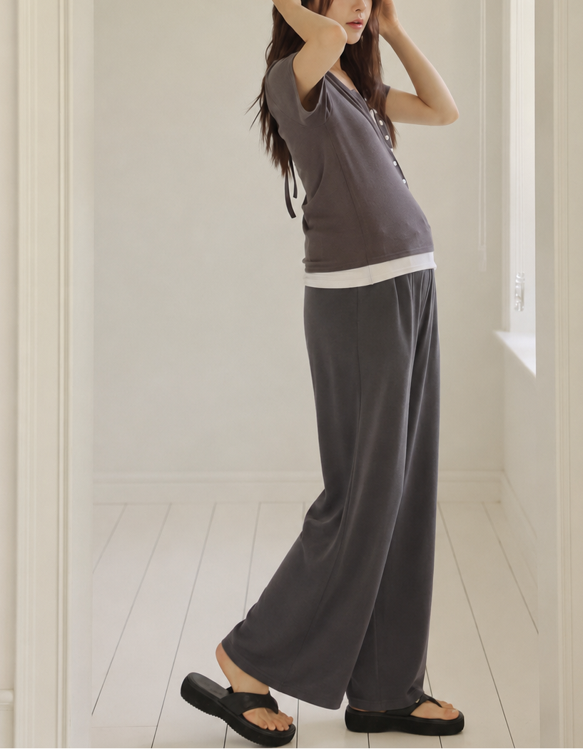 Woman in a gray outfit standing in a room with white walls and a window.