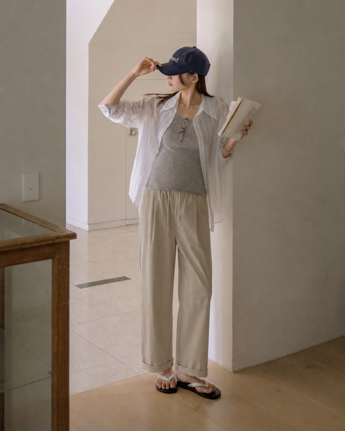Woman in casual outfit holding a book in a minimal indoor setting