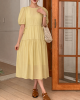 Woman wearing a yellow dress standing in a room with wooden flooring and a door.