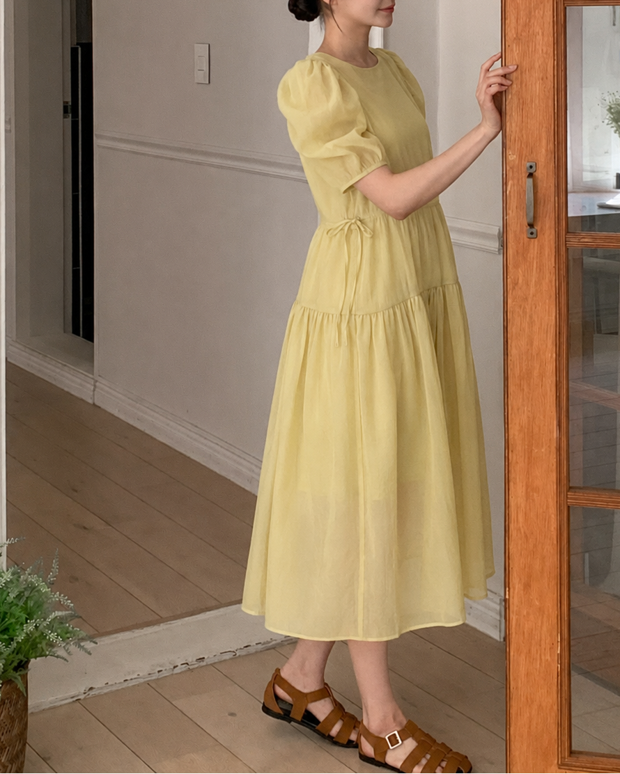Woman in a yellow dress standing in a home interior.