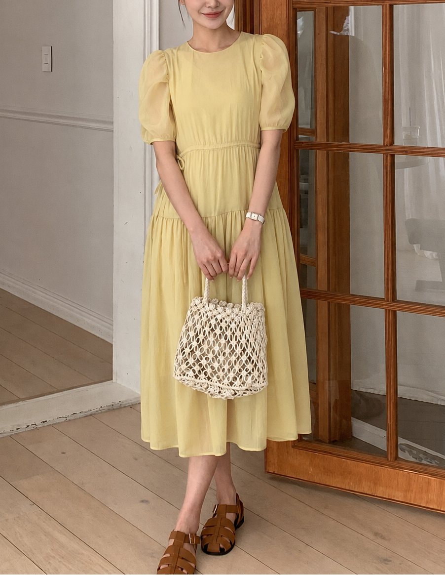 Woman in a yellow dress holding a woven bag indoors.